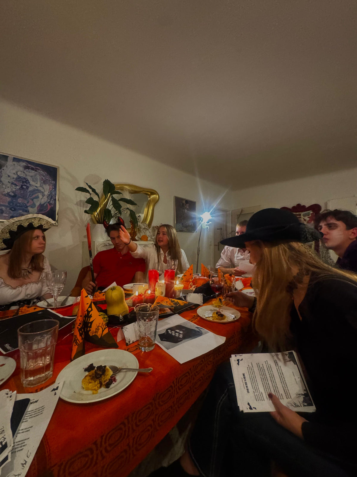 Gäste in Halloween-Kostümen spielen Spuk in der Scheune an einer orange gedeckten Tafel mit Kerzen